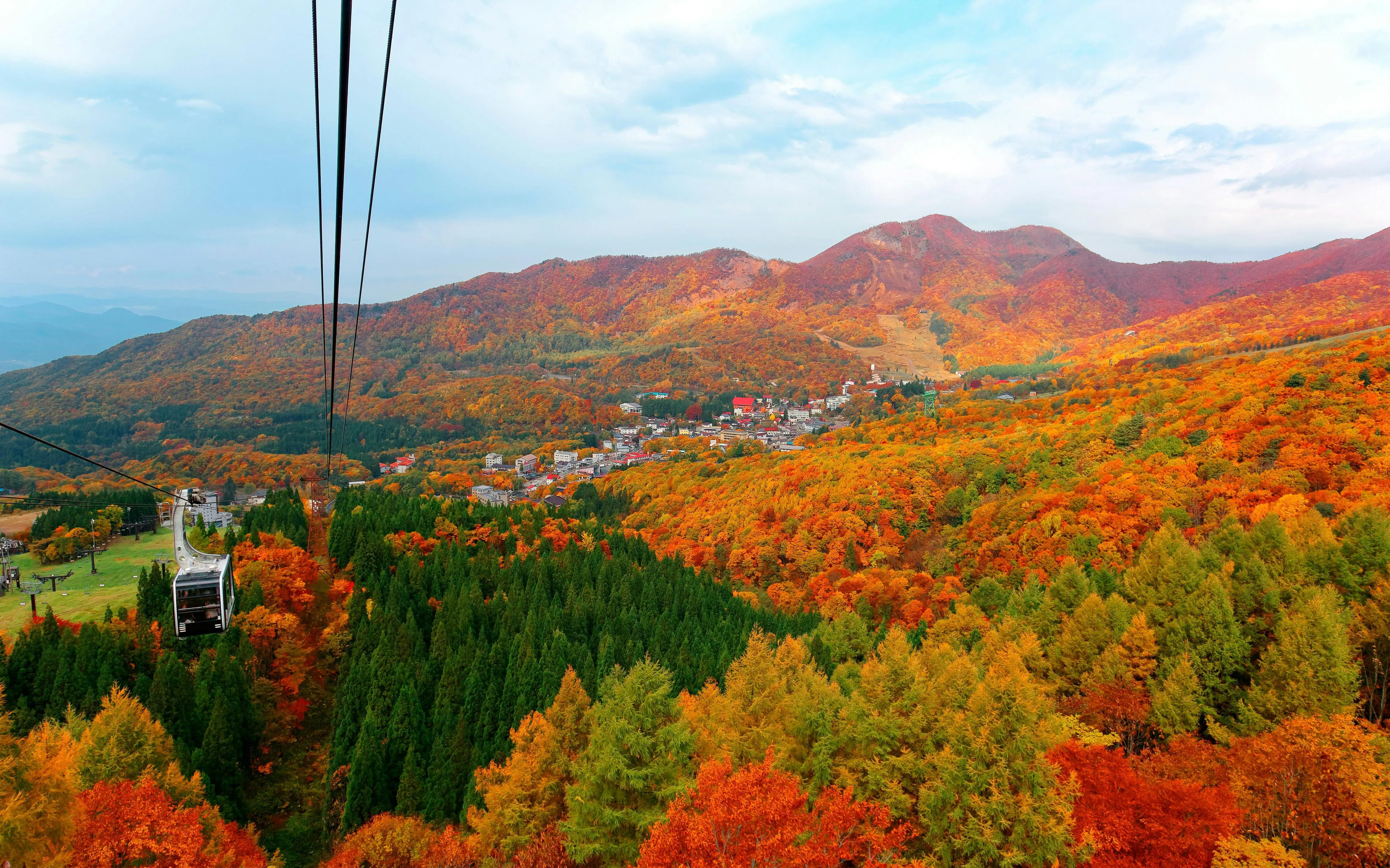 Cable car over autumn foliage in Zao, Yamagata, Japan, with mountains and resort below.