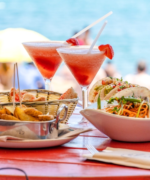 Beachfront dining setup with tables and chairs under umbrellas, ocean view in the background, Maldives.