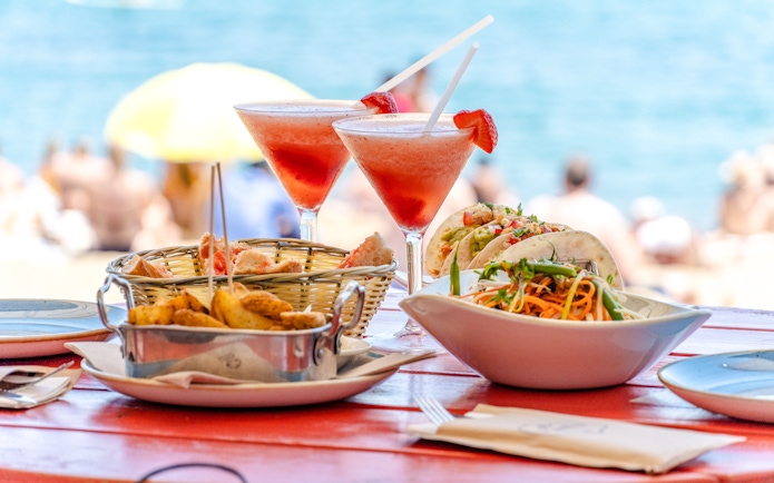 Beachfront dining setup with tables and chairs under umbrellas, ocean view in the background, Maldives.