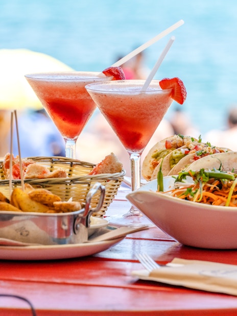 Beachfront dining setup with tables and chairs under umbrellas, ocean view in the background, Maldives.