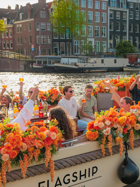 Guests enjoying drinks on a flower-adorned boat during a canal cruise in Amsterdam.