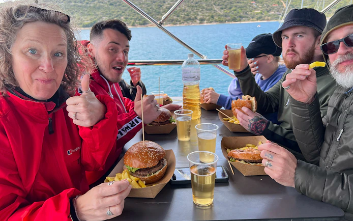 Group enjoying lunch on a cruise near Split, with burgers, fries, and drinks.