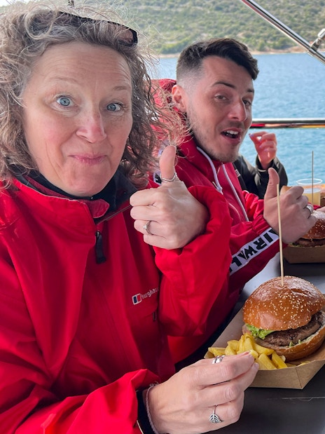 Group enjoying lunch on a cruise near Split, with burgers, fries, and drinks.