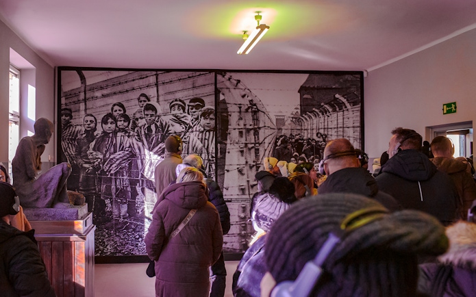 Visitors viewing historical photo inside Auschwitz-Birkenau Memorial Museum during guided tour.