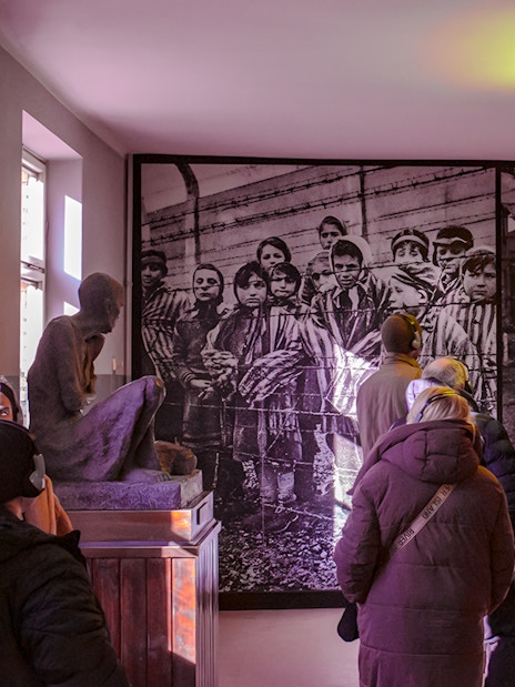 Visitors viewing historical photo inside Auschwitz-Birkenau Memorial Museum during guided tour.