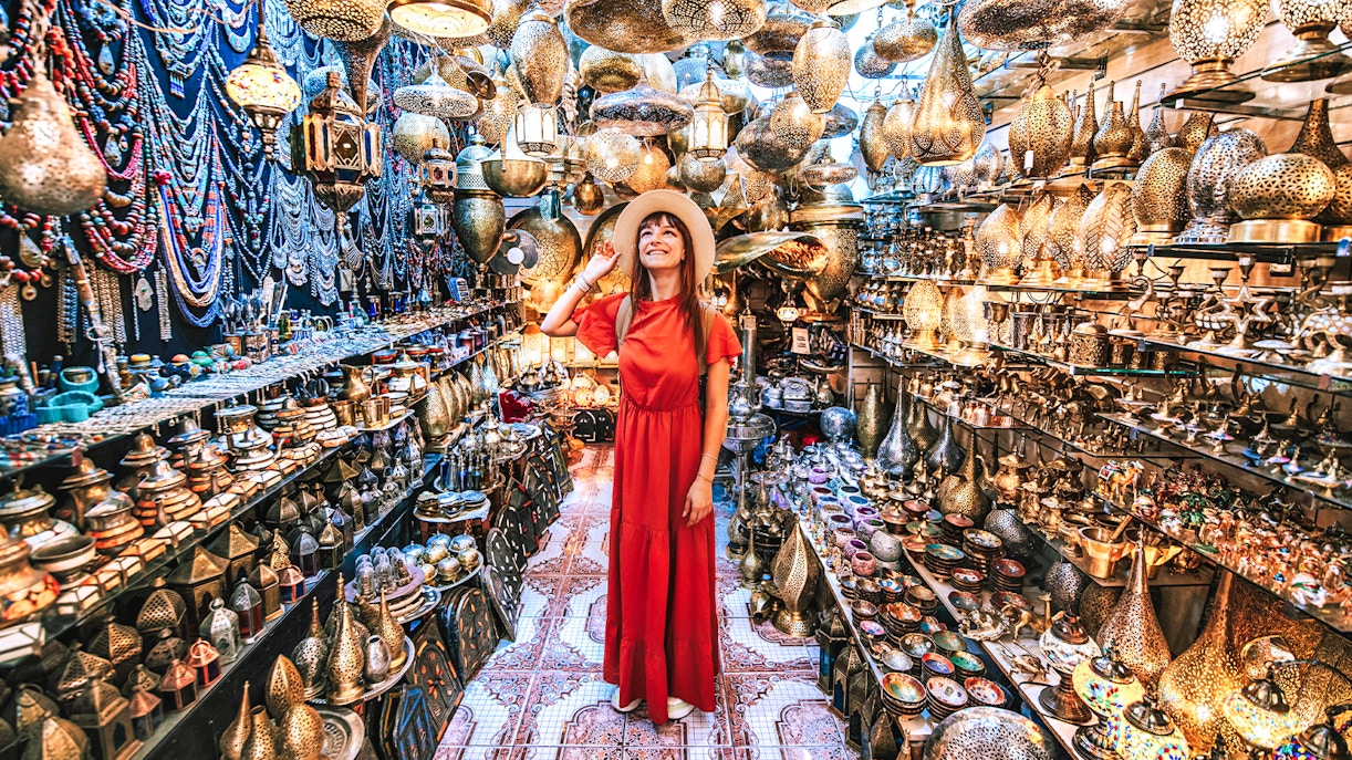 Woman exploring a copper souvenir shop in Marrakesh, surrounded by intricate lamps and crafts.