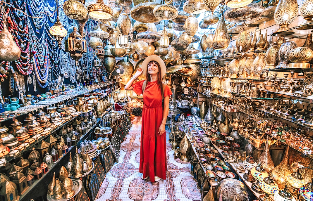 Woman exploring a copper souvenir shop in Marrakesh, surrounded by intricate lamps and crafts.