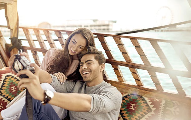 Couple taking a selfie on an abra boat during Burj Khalifa sunset tour in Dubai.