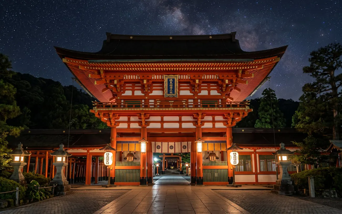 Fushimi Inari shrine entrance illuminated at night, Kyoto, with lanterns and torii gates.