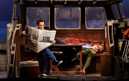 Man reading newspaper on boat set of "The Shark is Broken" play.
