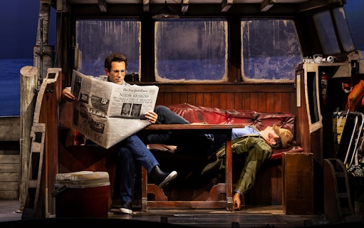 Man reading newspaper on boat set of "The Shark is Broken" play.