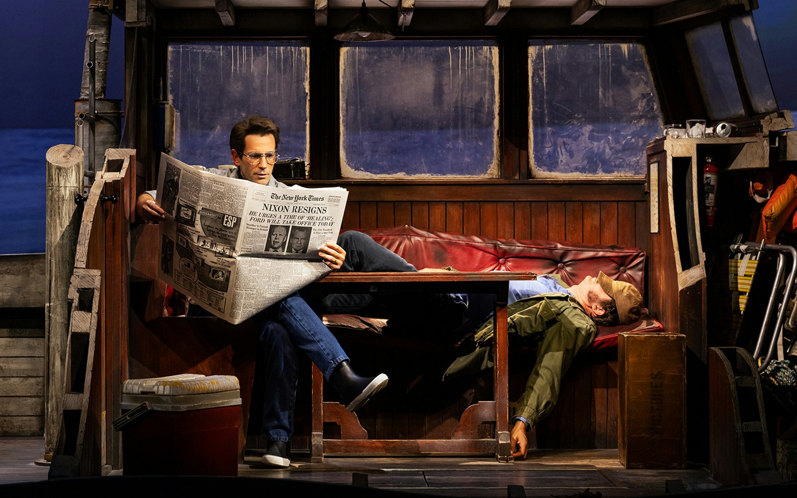 Man reading newspaper on boat set of "The Shark is Broken" play.