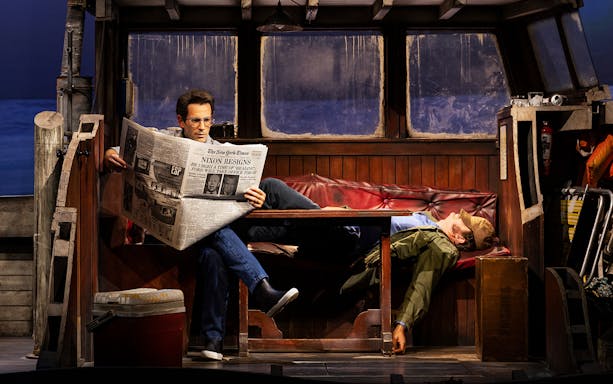 Man reading newspaper on boat set of "The Shark is Broken" play.