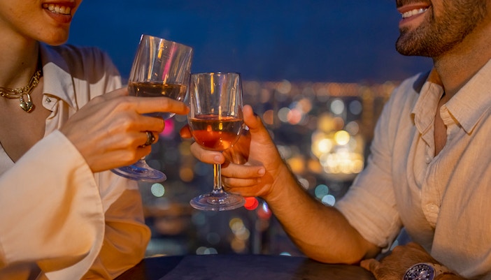 Couple toasting with wine glasses at a rooftop restaurant overlooking city lights.