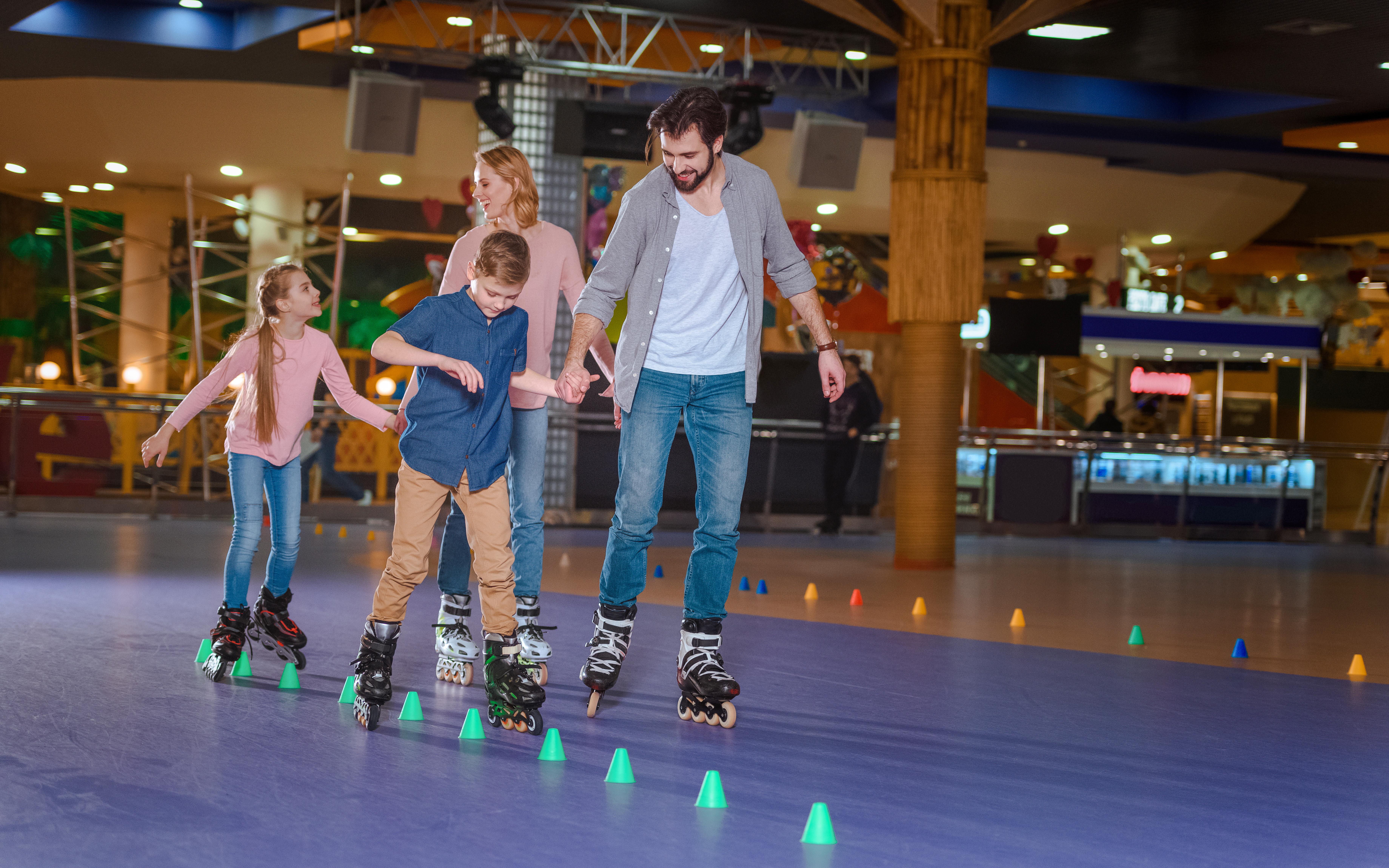 Family roller skating together on indoor rink with colorful cones.