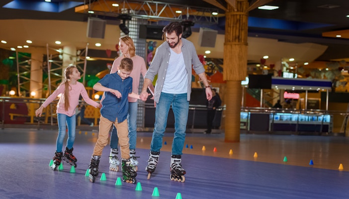 Family roller skating together on indoor rink with colorful cones.