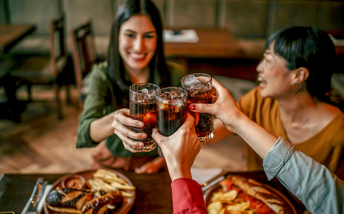 Friends toasting with drinks at a restaurant table with food.