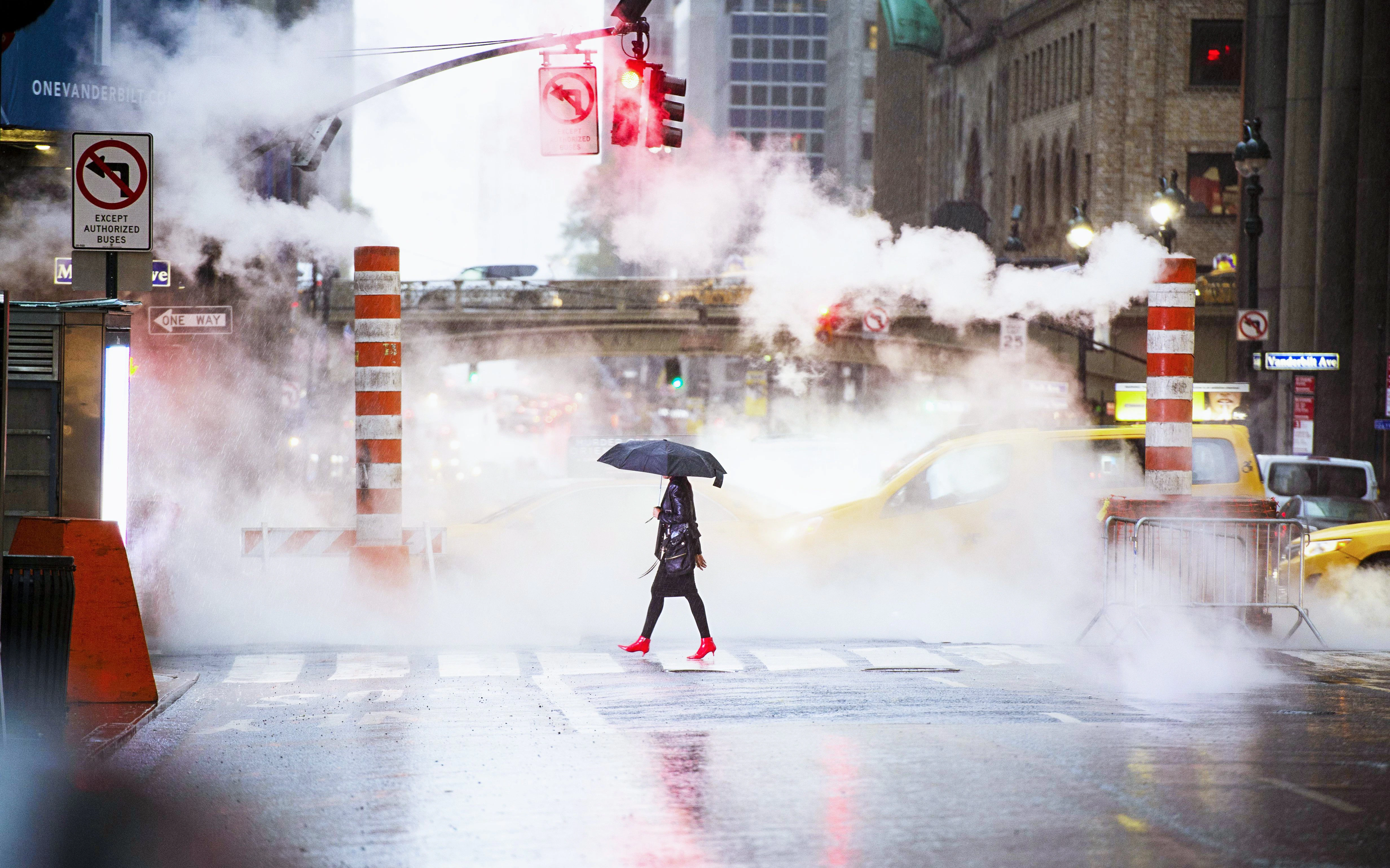 Woman with umbrella and red heels crossing 42nd Street, steam and cars in Manhattan, New York City.