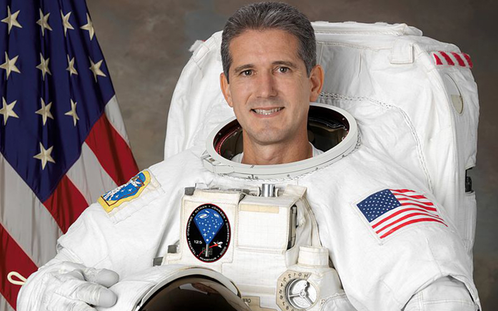 Astronaut Mike Good in space suit with Earth in the background.