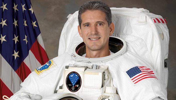 Astronaut Mike Good in space suit with Earth in the background.