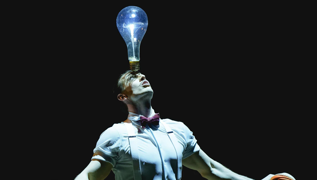 Performer balancing a glowing light bulb on head at Cirque du Soleil: Kurios, London.