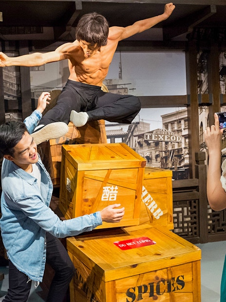 Man posing with Bruce Lee statue at Madame Tussauds Singapore, part of Go City Singapore Pass.
