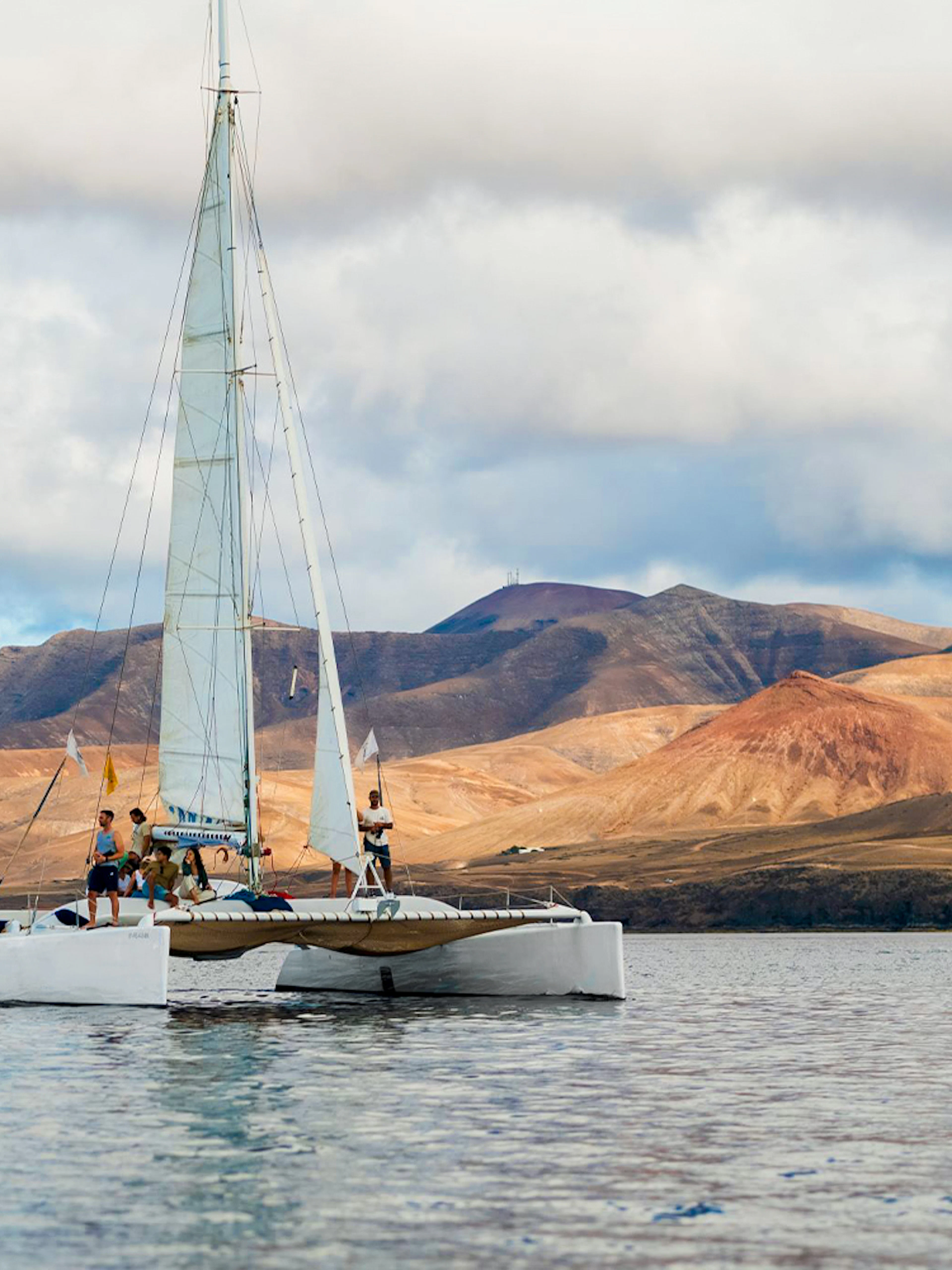 Tourists on a catamaran in Lanzarote waters with mountains in the background.