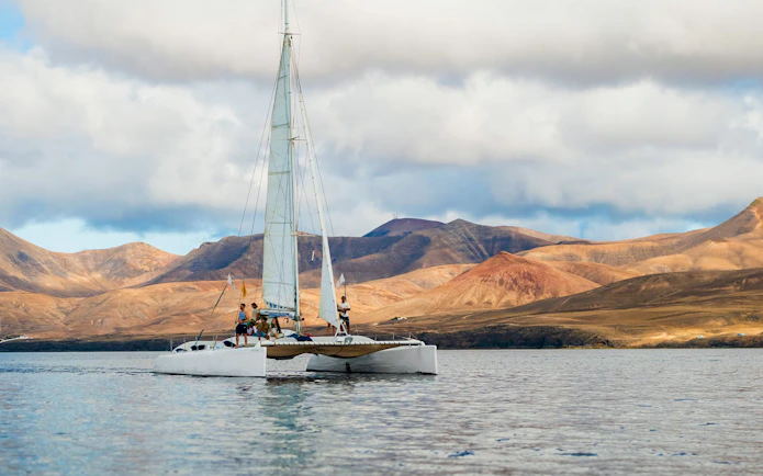 Tourists on a catamaran in Lanzarote waters with mountains in the background.