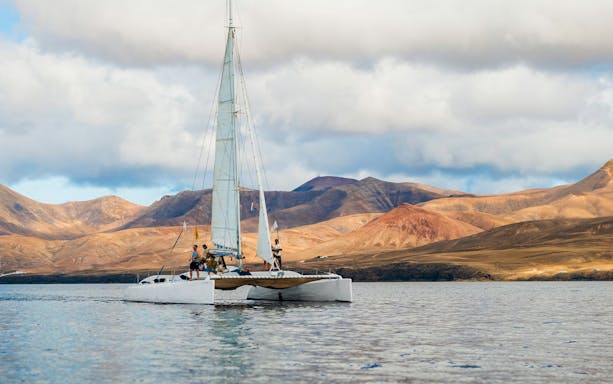 Tourists on a catamaran in Lanzarote waters with mountains in the background.