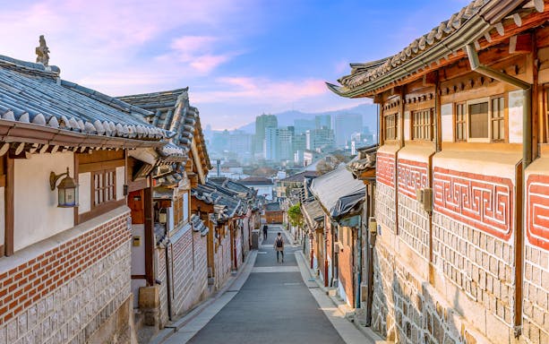 Hanok Village in Seoul with traditional Korean architecture and city skyline in the background.