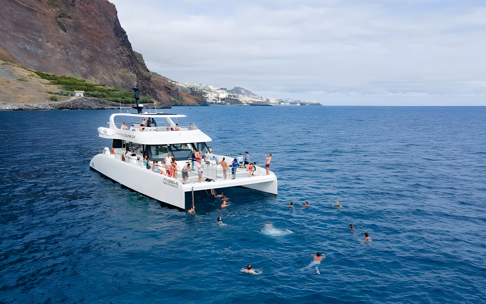 Catamaran with tourists swimming near Funchal coast on dolphin and whale watching tour.