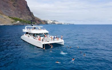Catamaran with tourists swimming near Funchal coast on dolphin and whale watching tour.