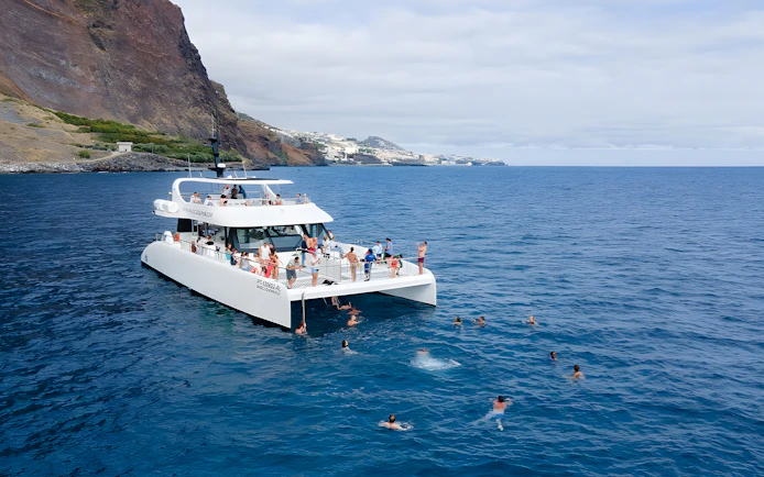Catamaran with tourists swimming near Funchal coast on dolphin and whale watching tour.