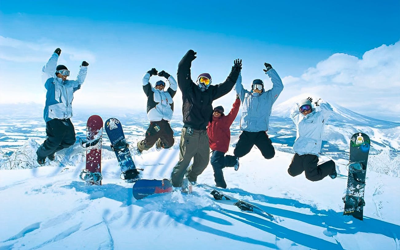 Group of snowboarders jumping on snowy mountain at Niseko Resort, Japan.