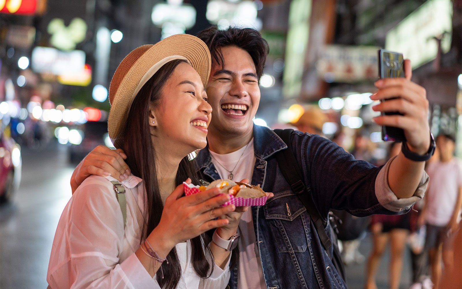 Couple enjoying street food and taking a selfie in Tokyo at night.