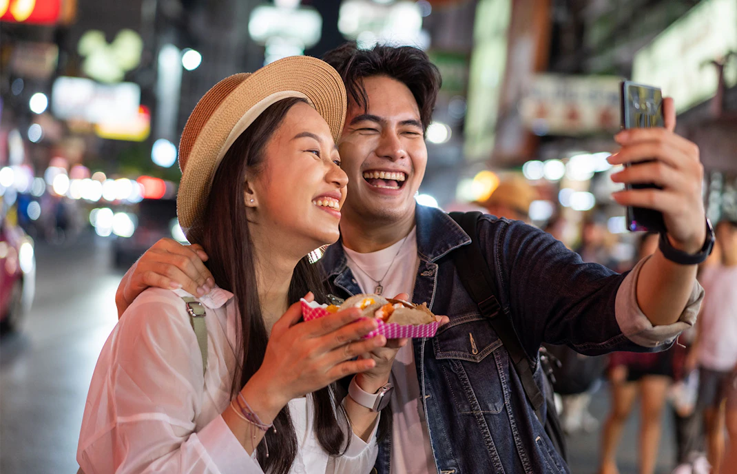 Couple enjoying street food and taking a selfie in Tokyo at night.