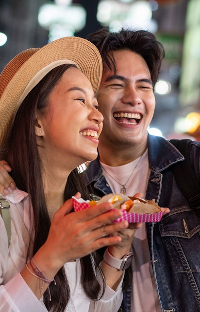 Couple enjoying street food and taking a selfie in Tokyo at night.