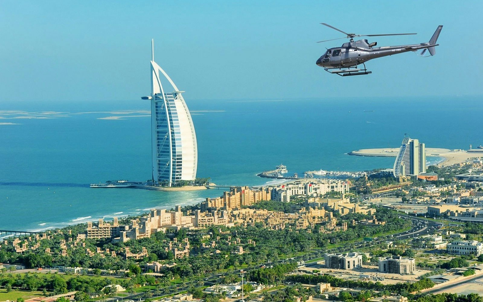 Helicopter flying near Burj Al Arab, Dubai coastline in view.