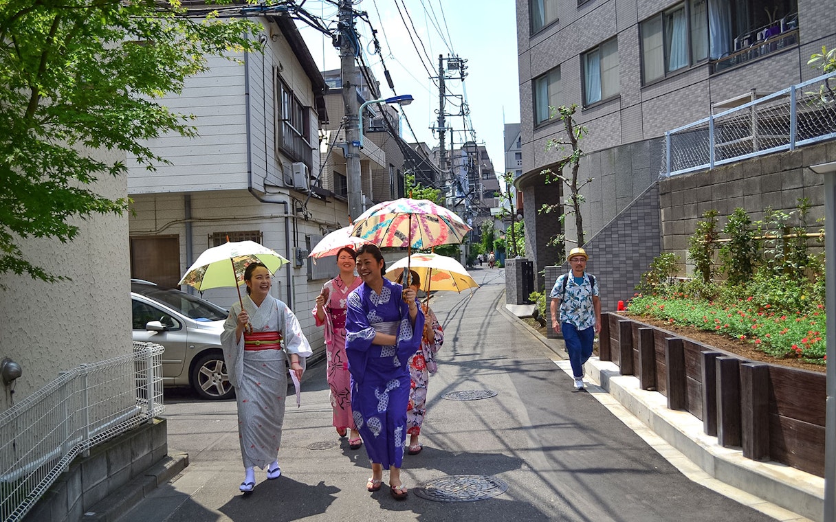 Women in kimonos walking with umbrellas in a Japanese street.