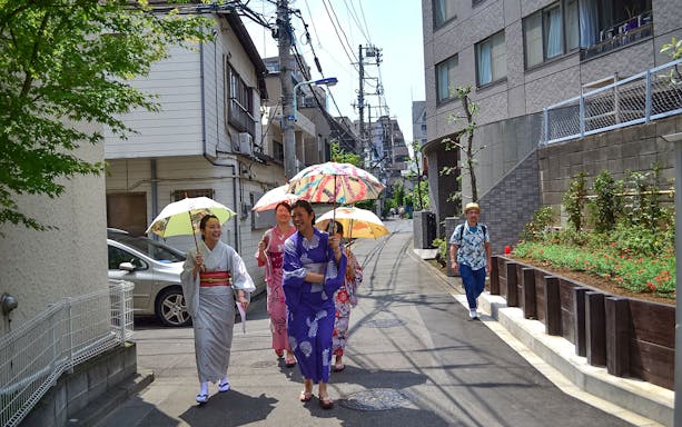 Women in kimonos walking with umbrellas in a Japanese street.