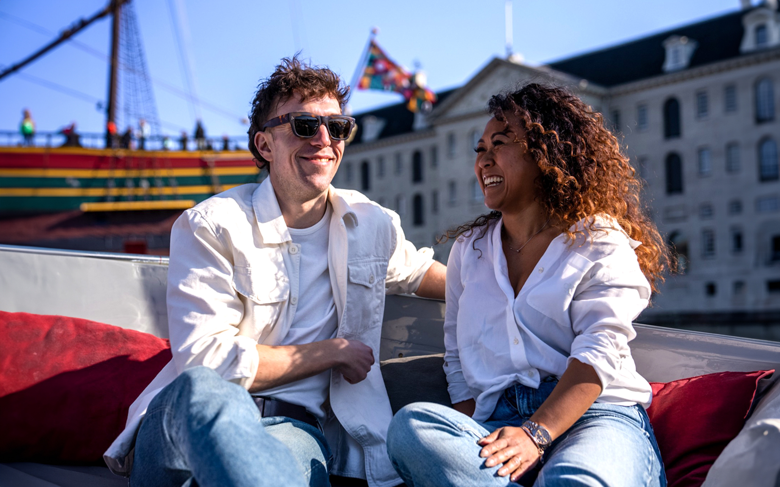 Couple enjoying Amsterdam Light Festival cruise with historic ship in background.