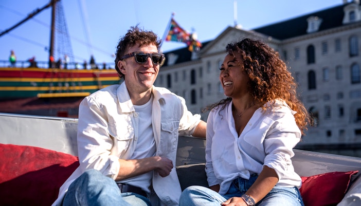 Couple enjoying Amsterdam Light Festival cruise with historic ship in background.