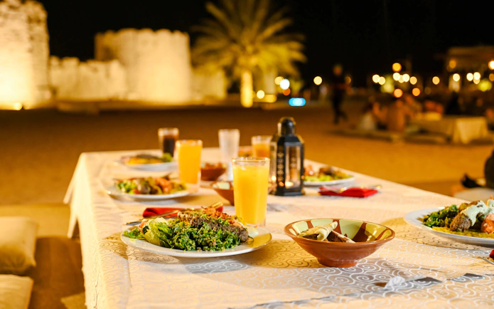 Meal setup at Dubai desert safari with plates of food and drinks on a table.