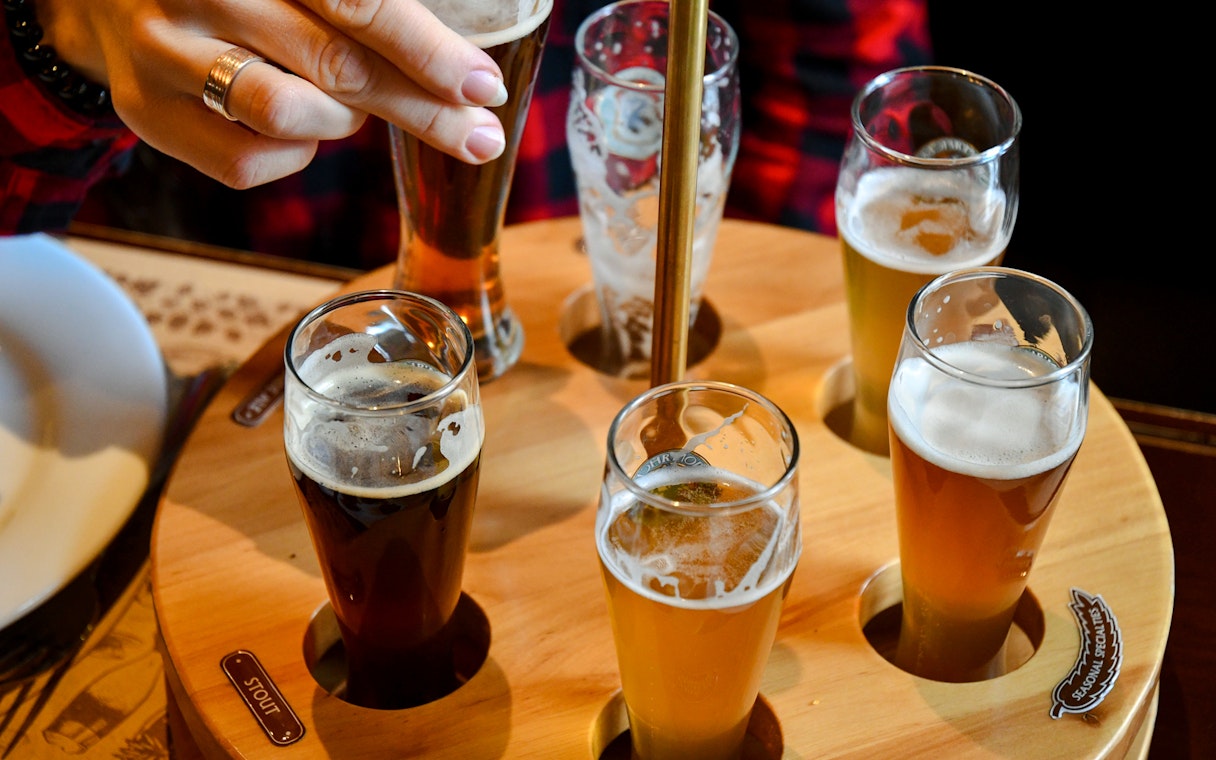 Beer flight with various beers in small glasses on a wooden tray.