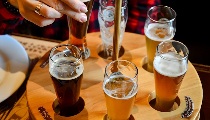 Beer flight with various beers in small glasses on a wooden tray.