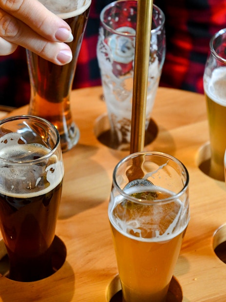 Beer flight with various beers in small glasses on a wooden tray.