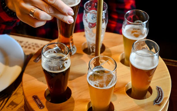 Beer flight with various beers in small glasses on a wooden tray.