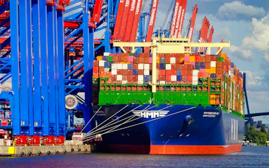 Container ship docked at Hamburg harbor with cranes and colorful containers.