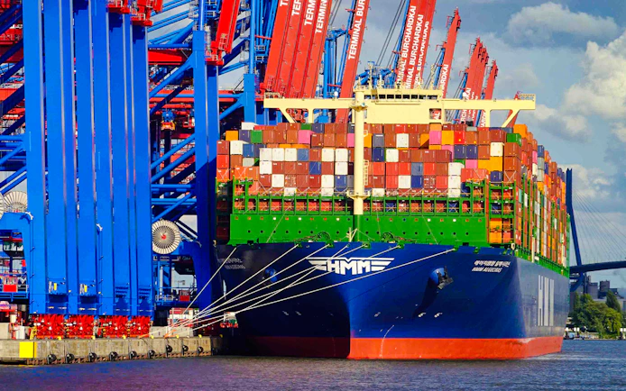 Container ship docked at Hamburg harbor with cranes and colorful containers.