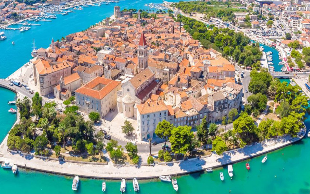 Aerial view of Trogir's historic center with red-roofed buildings and surrounding turquoise waters.